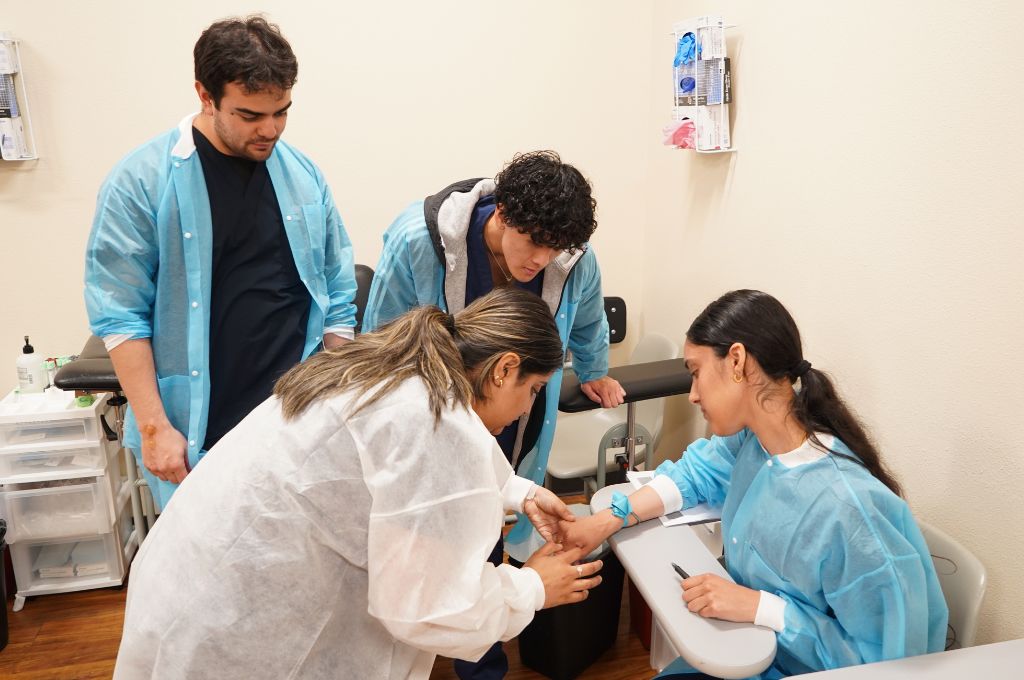 Phlebotomy technician students practicing a blood draw under instructor supervision.