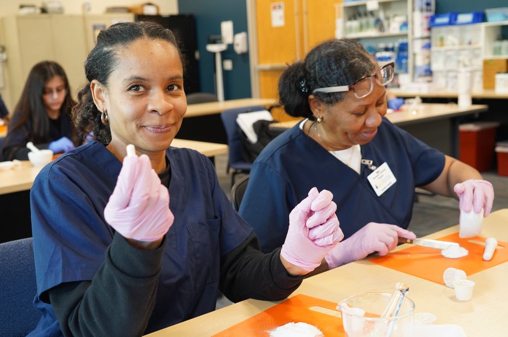 Two pharmacy technician students in California prepare medication during hands-on lab training.