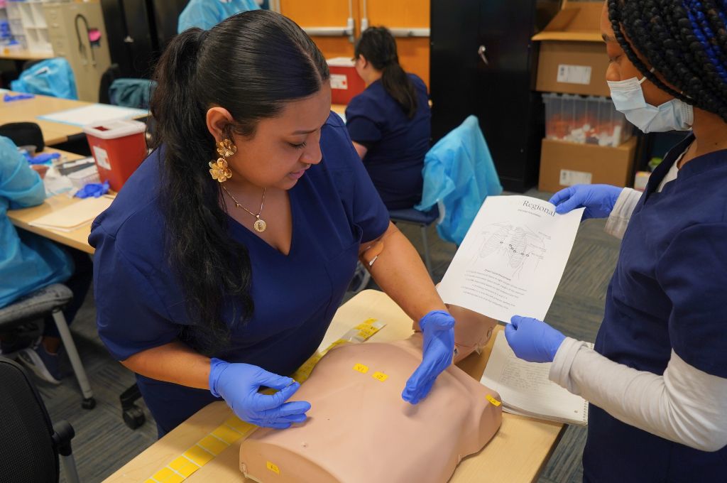 Healthcare training students practicing EKG techniques using a medical simulation model.