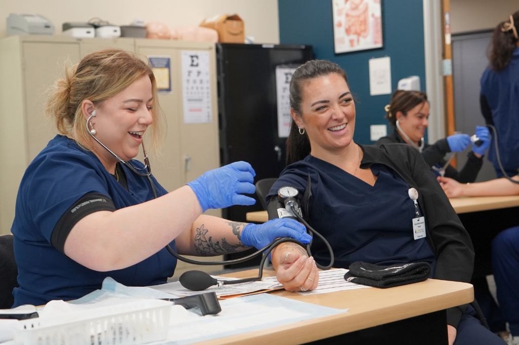 Students practicing blood pressure measurement during hands-on clinical healthcare training.