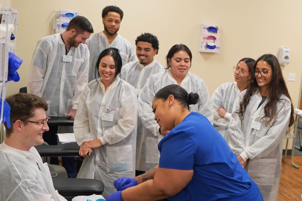 Phlebotomy instructor demonstrating blood draw techniques to students in a training setting.
